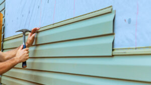 A worker hammers in a nail to install green siding on an exterior wall of a house? actually this is a description need no question marks. I'll correct. A worker hammers in a nail to install green siding on an exterior wall of a house.